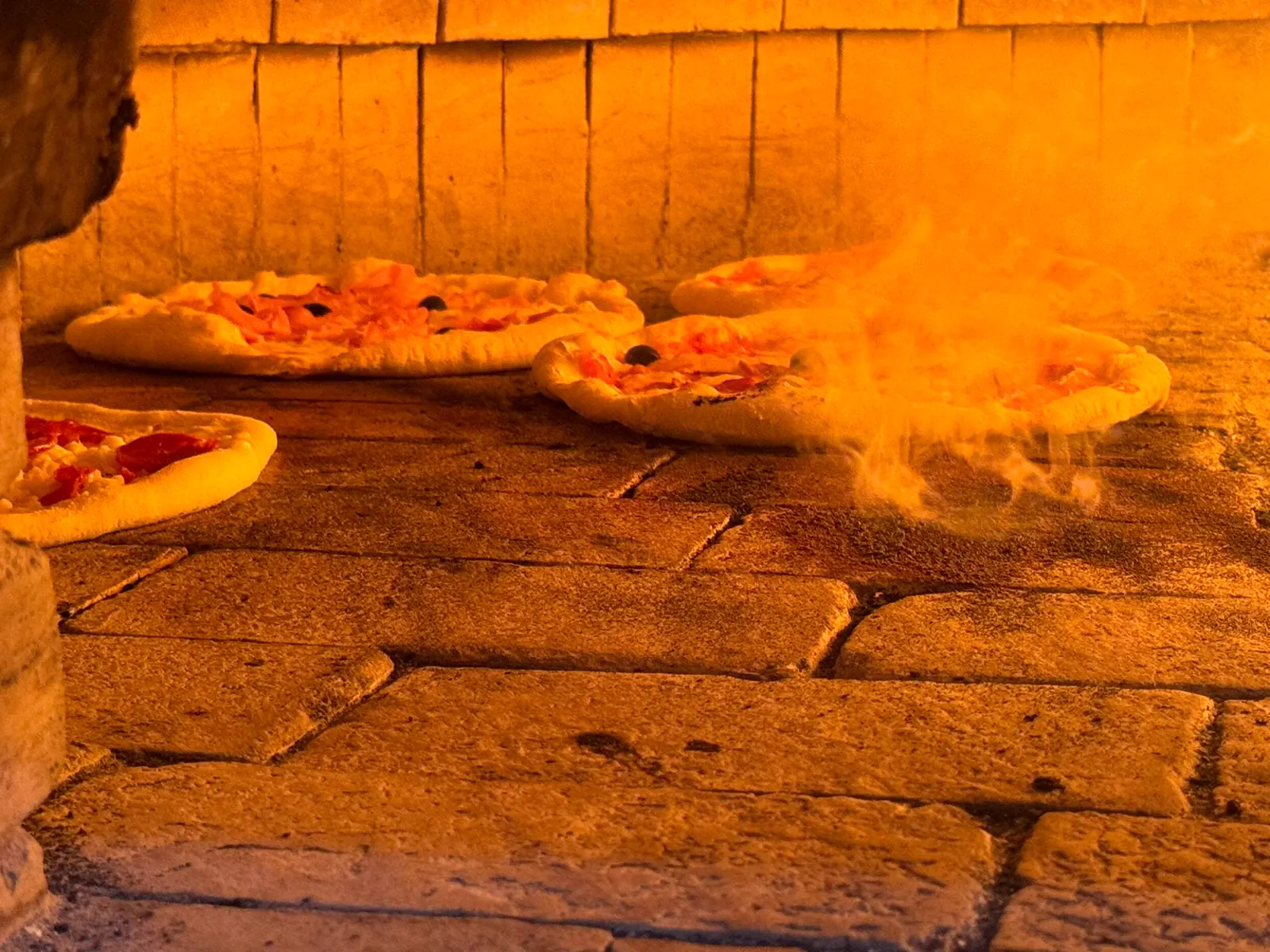 Pizze in cottura sul piano refrattario del forno a legna