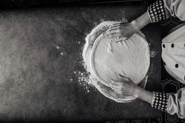 Le mani del pizzaiolo che stendono l'impasto sulla farina